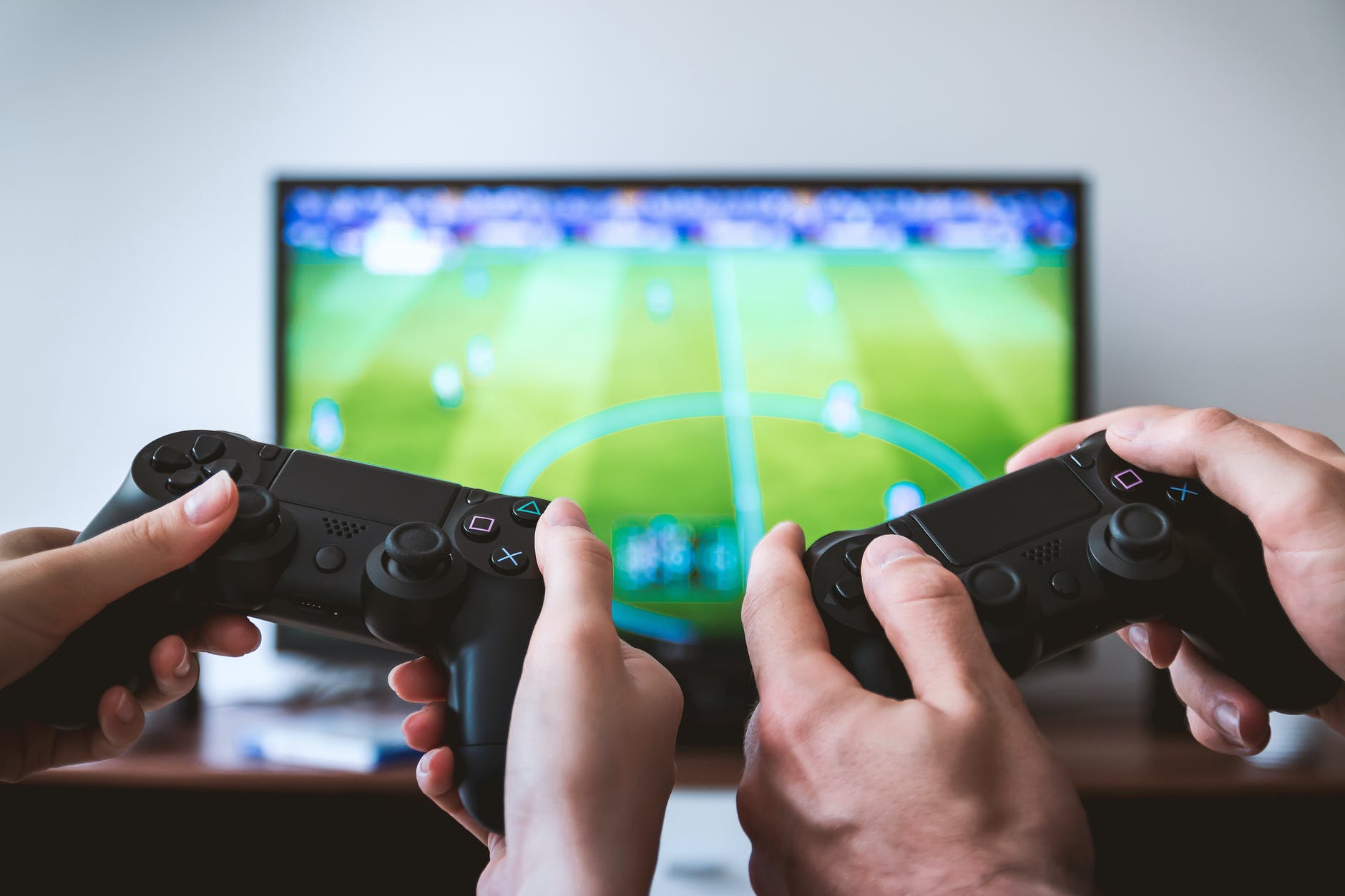 Two people holding playstation controllers infront of a TV